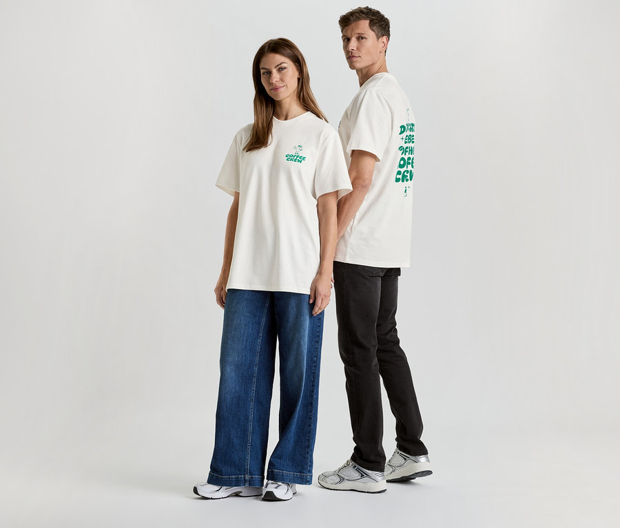 Eine Frau in Jeans und ein Mann in schwarzer Hose, beide tragen weiße T-Shirts mit Aufdruck.