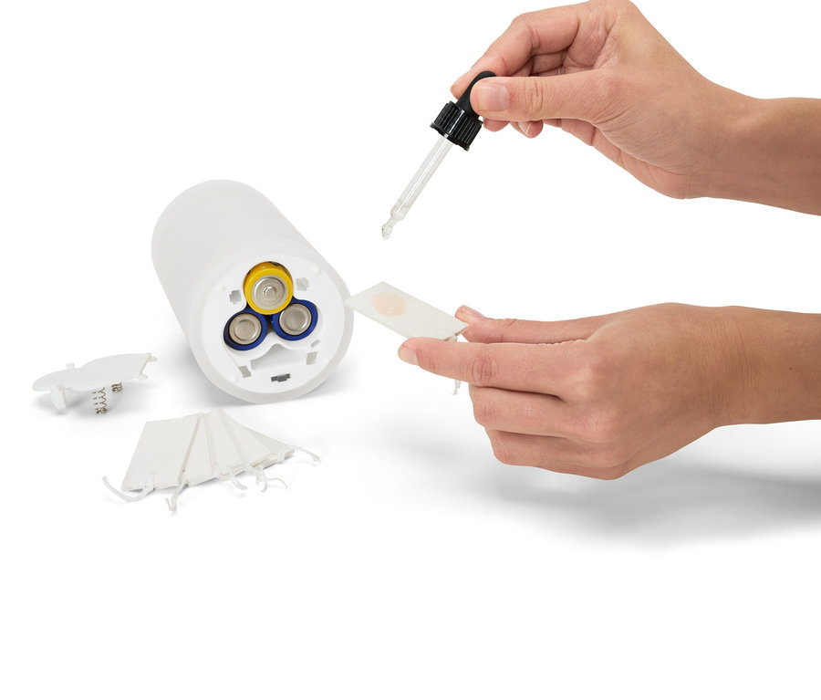 Eine Hand tropft Flüssigkeit aus einer Pipette auf einen weißen Duftspender, der mit Batterien betrieben wird.