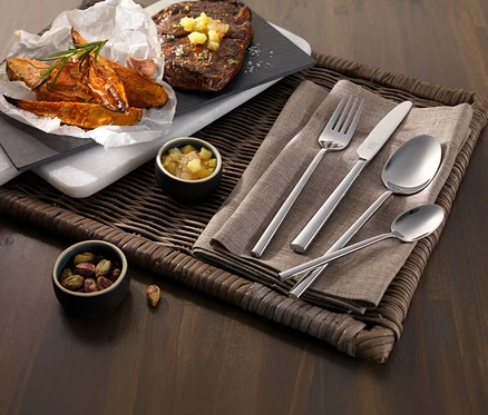 Ein Gericht mit Steak, Süßkartoffelspalten und einem ZWILLING »Aberdeen« Besteck-Set auf einem geflochtenen Tablett. Dazu kleine Schalen mit Salsa und Pistazien.