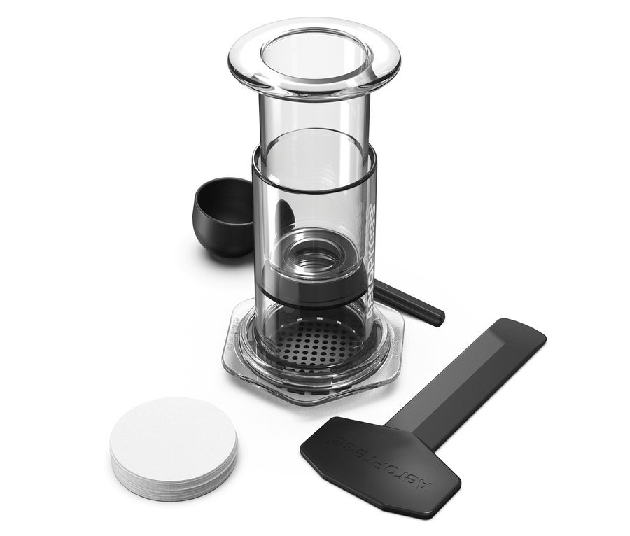 Nahaufnahme eines Aeropress Kaffeebereiters mit Zubehör wie einem Messlöffel, einem Rührstab, einem Schaber und Papierfiltern.