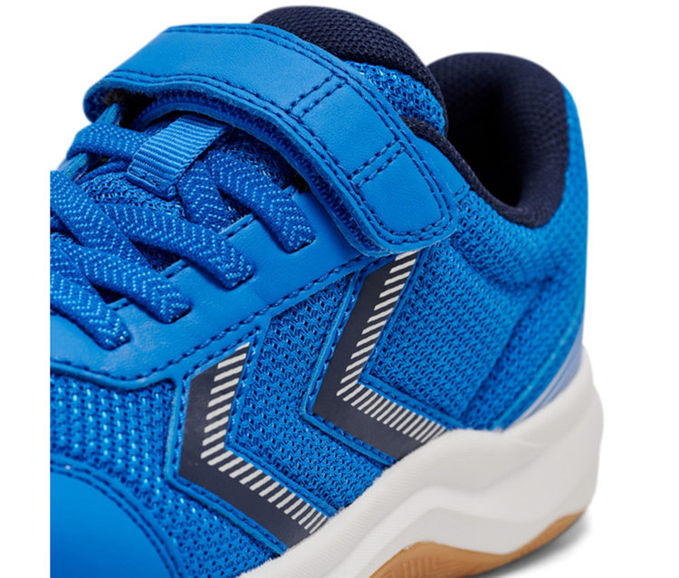 Nahaufnahme eines blauen Sneakers mit Mesh- und Kunstlederdetails. Er hat blaue Schnürsenkel, einen blauen Klettverschluss und ein weiß-dunkelblau gestreiftes Logo an der Seite. Die Sohle ist weiß mit einer braunen Laufsohle.