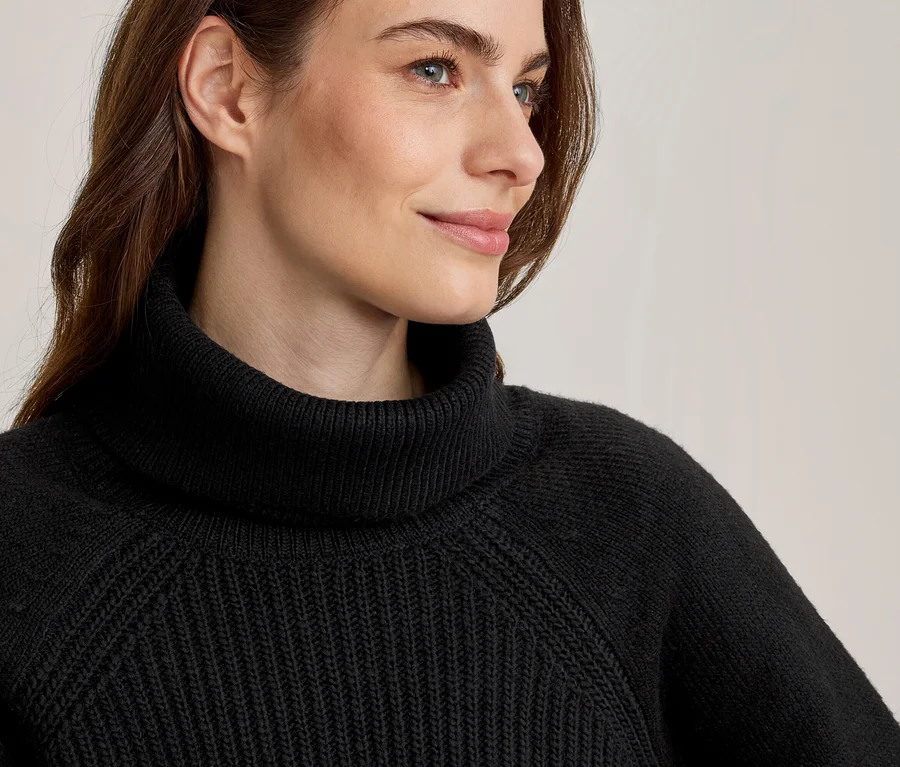 Nahaufnahme einer Frau in einem schwarzen Rollkragenpullover mit Rippstrickmuster, die nach rechts blickt.