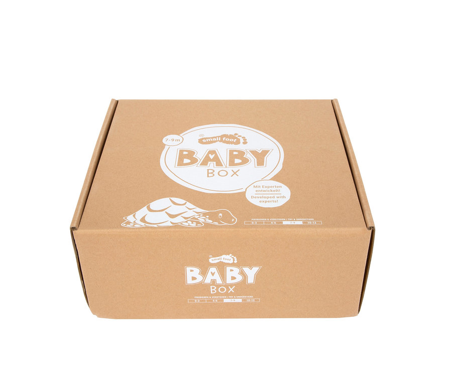 Eine hellbraune Kartonschachtel mit weißem "small foot BABY BOX"-Branding, einer Schildkrötengrafik und dem Text "PROBIEREN & VERSTEHEN | TRY & UNDERSTAND" mit Altersbereichen "0-3" bis "10-12" auf Oberseite und Vorderseite. Oben steht auch "Mit Experten entwickelt!".