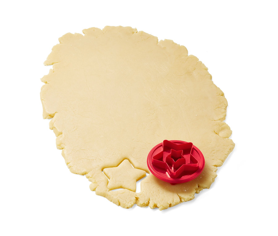 Ein roter 3 Linzer-Plätzchen-Ausstecher liegt auf einem Teig, aus dem ein Stern ausgestochen wurde.