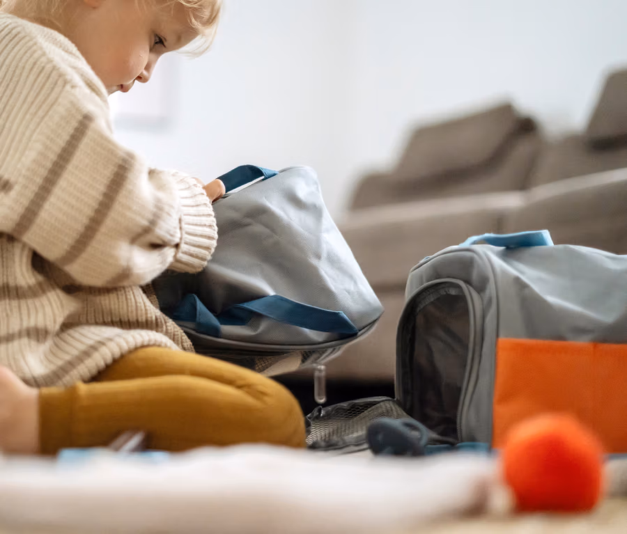 Kind sitzt am Boden und spielt mit einer grauen Tasche und Spielzeug, darunter ein 'small foot Katze mit Tasche und Pflege-Set'.