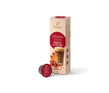 Eine beige Schachtel Cafissimo Flavoured Espresso Maple & Pecan (10 Kapseln) steht aufrecht, davor liegt eine einzelne dunkelrote Kapsel. Die Schachtel zeigt ein Kaffeegetränk, Ahornblätter und Pekannüsse.