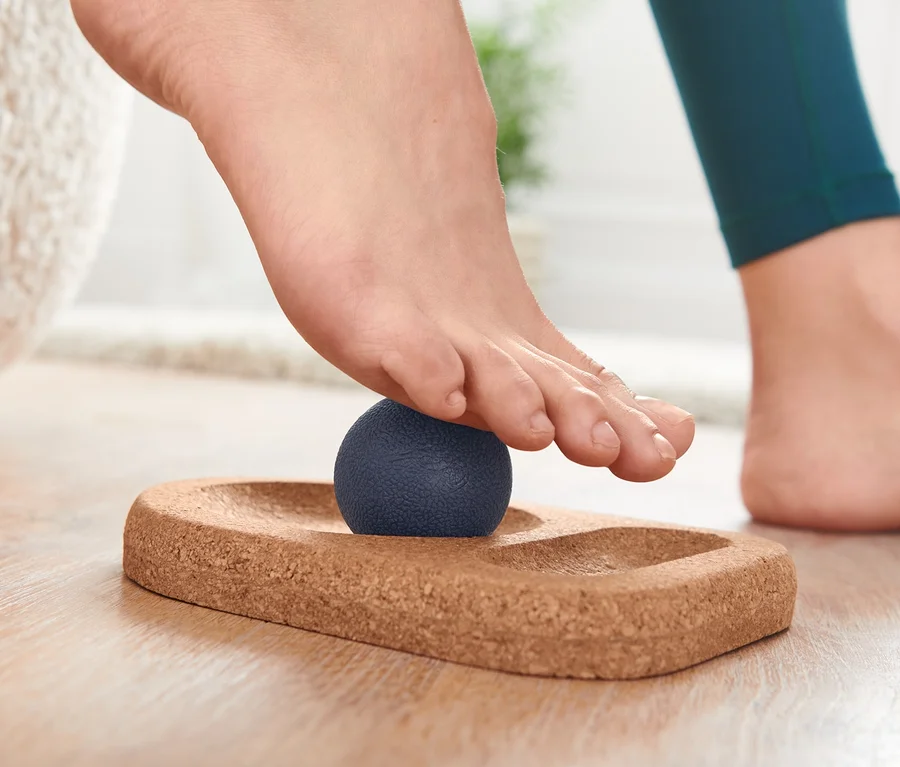 Fuß auf Fußmassageset mit blauem Massageball auf Korkunterlage.