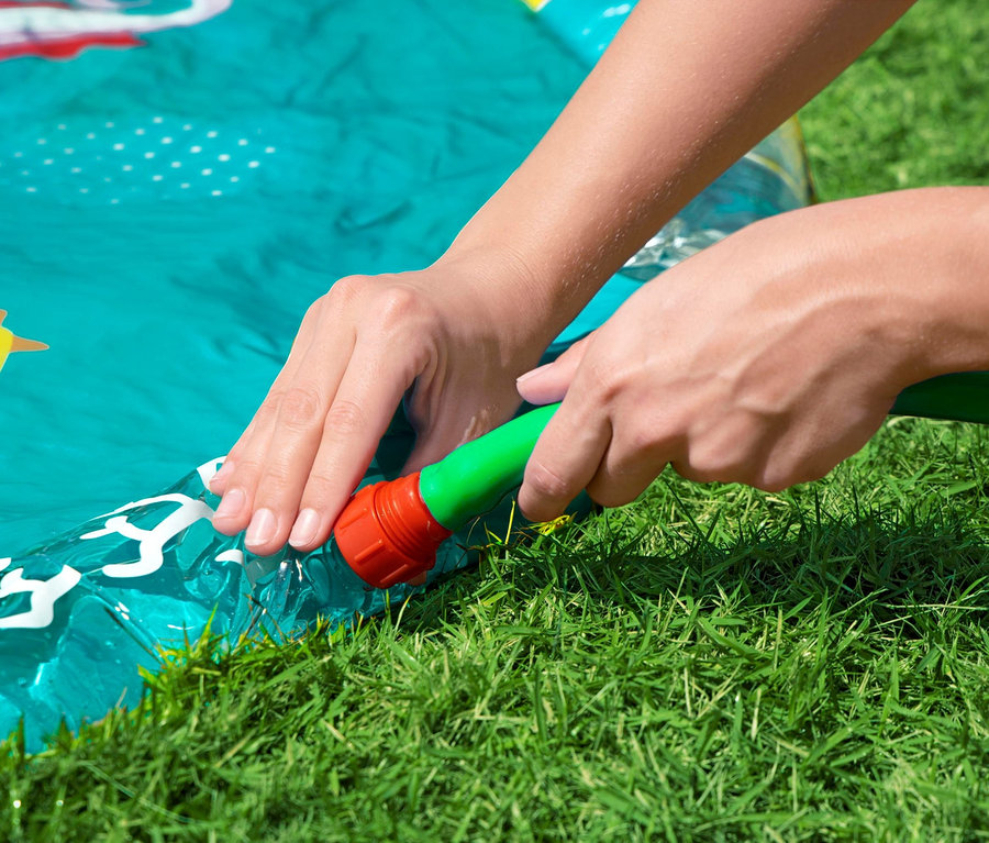 Person befüllt Bestway® Underwater Splash Pad mit einem Gartenschlauch auf Gras.