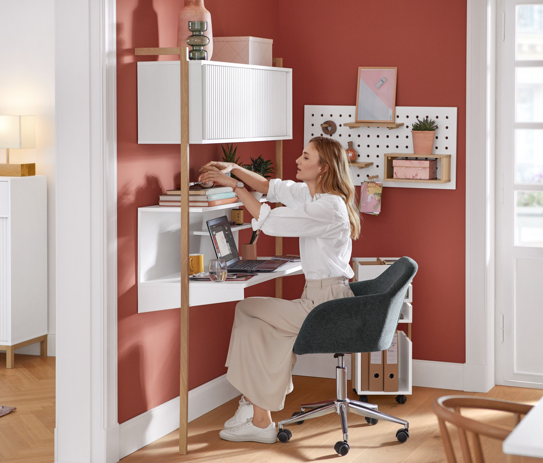 Eine Frau sitzt auf einem beigen Schreibtischstuhl an einem Schreibtisch-Regal und arbeitet an einem Laptop.