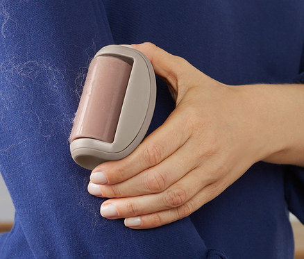 Frau entfernt mit einem Fusselroller Fusseln von einem blauen Pullover.