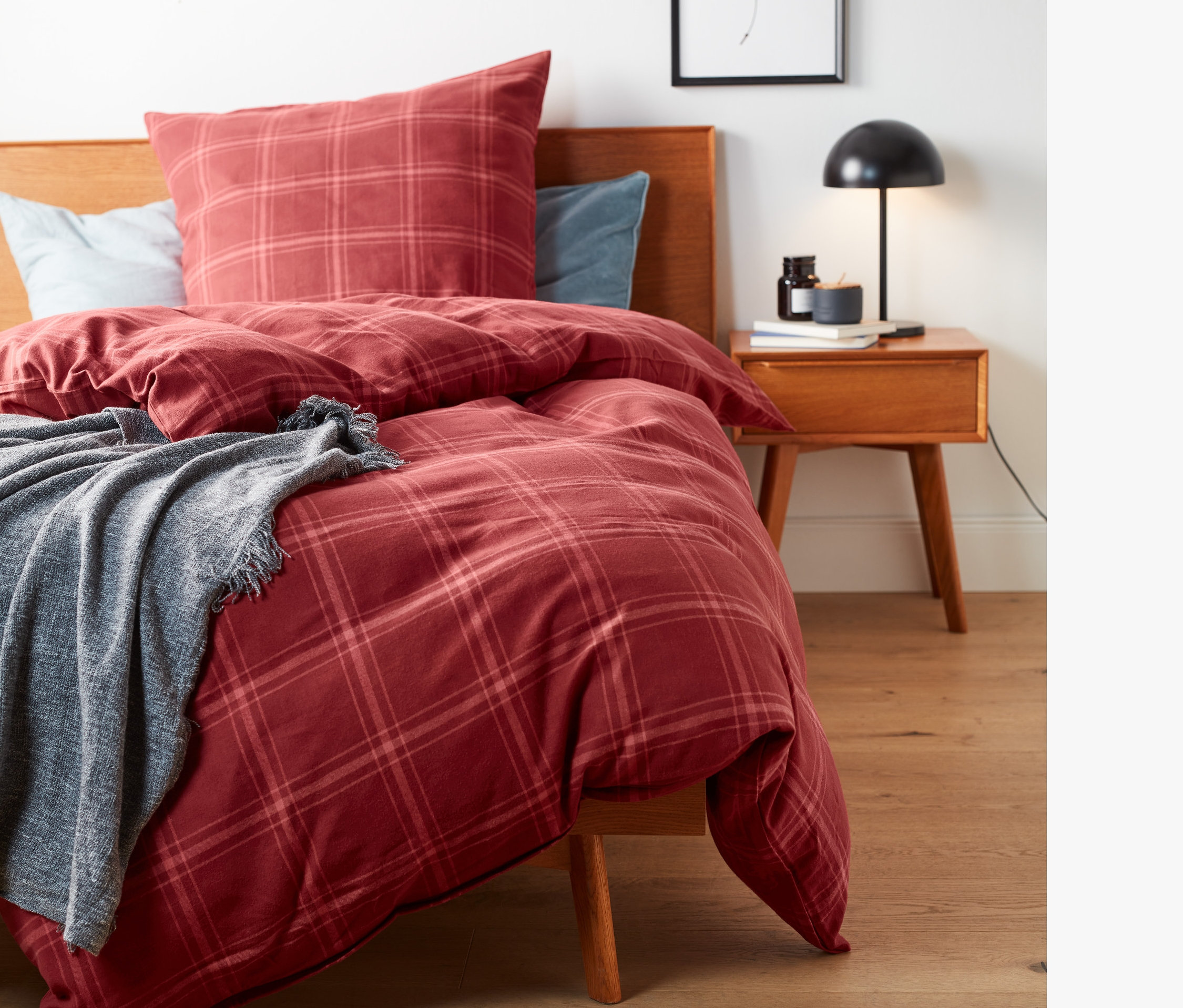 Rot karierte Flanell-Bettwäsche auf einem Bett mit Holzrahmen und grauer Decke.