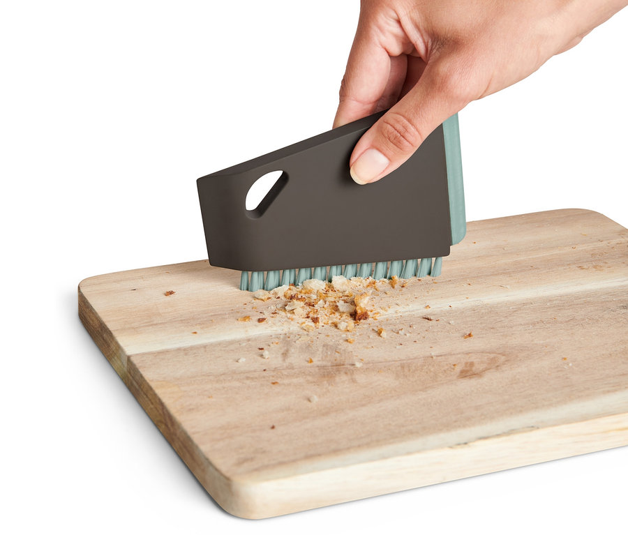 Eine Hand benutzt eine Universal-Küchenbürste, um Krümel von einem Holzbrett zu entfernen.