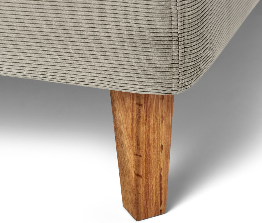 Detailaufnahme eines beigen Boxspringbetts mit Holzfuß.