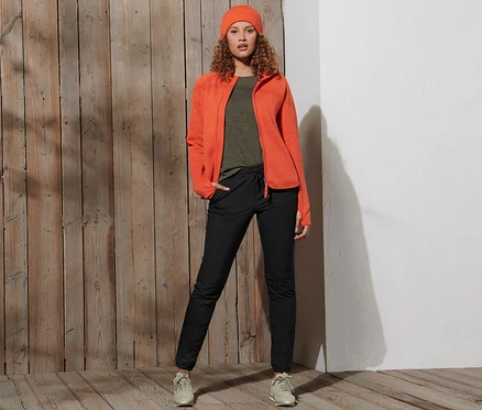 Frau posiert in orangefarbener Jacke und schwarzen Softshell-Joggpants.