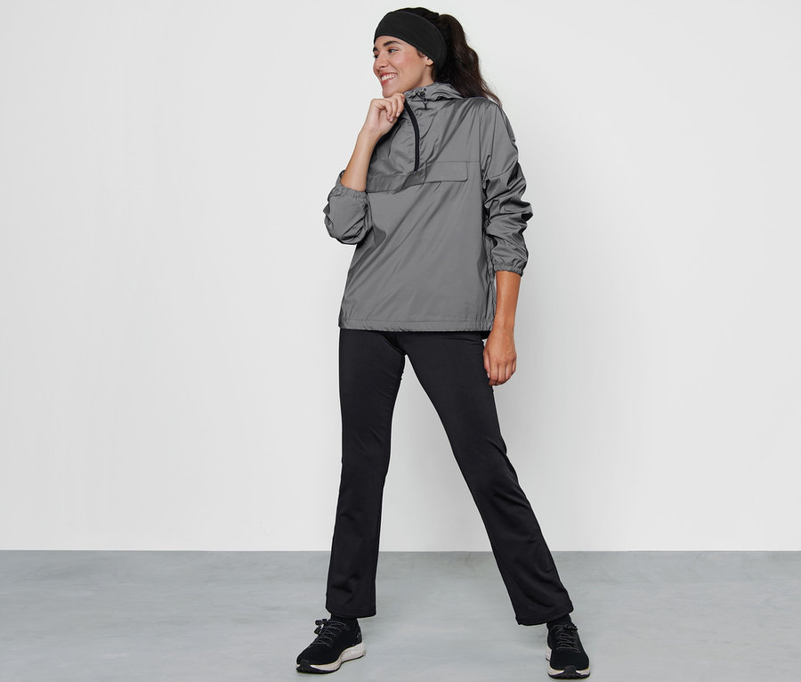 Frau posiert in reflektierendem Windbreaker, schwarzer Hose und Schuhen.