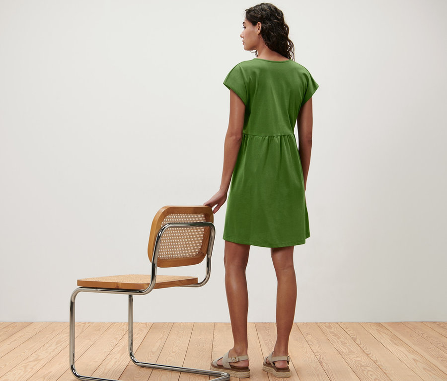 Frau von hinten in einem Jerseykleid, die Hand auf einem Stuhl.