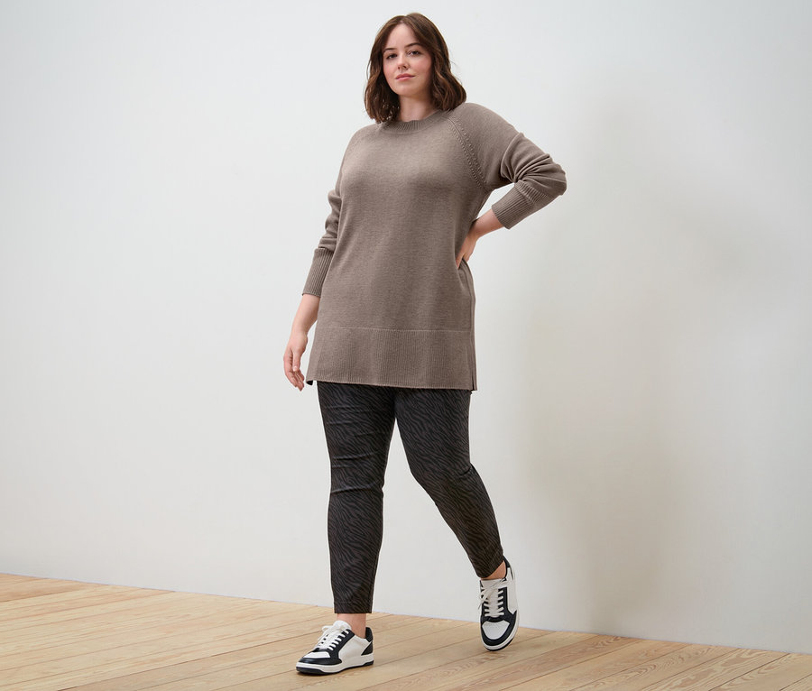 Frau posiert in langem Strickpullover in Taupe und einer Bengalin-Hose.