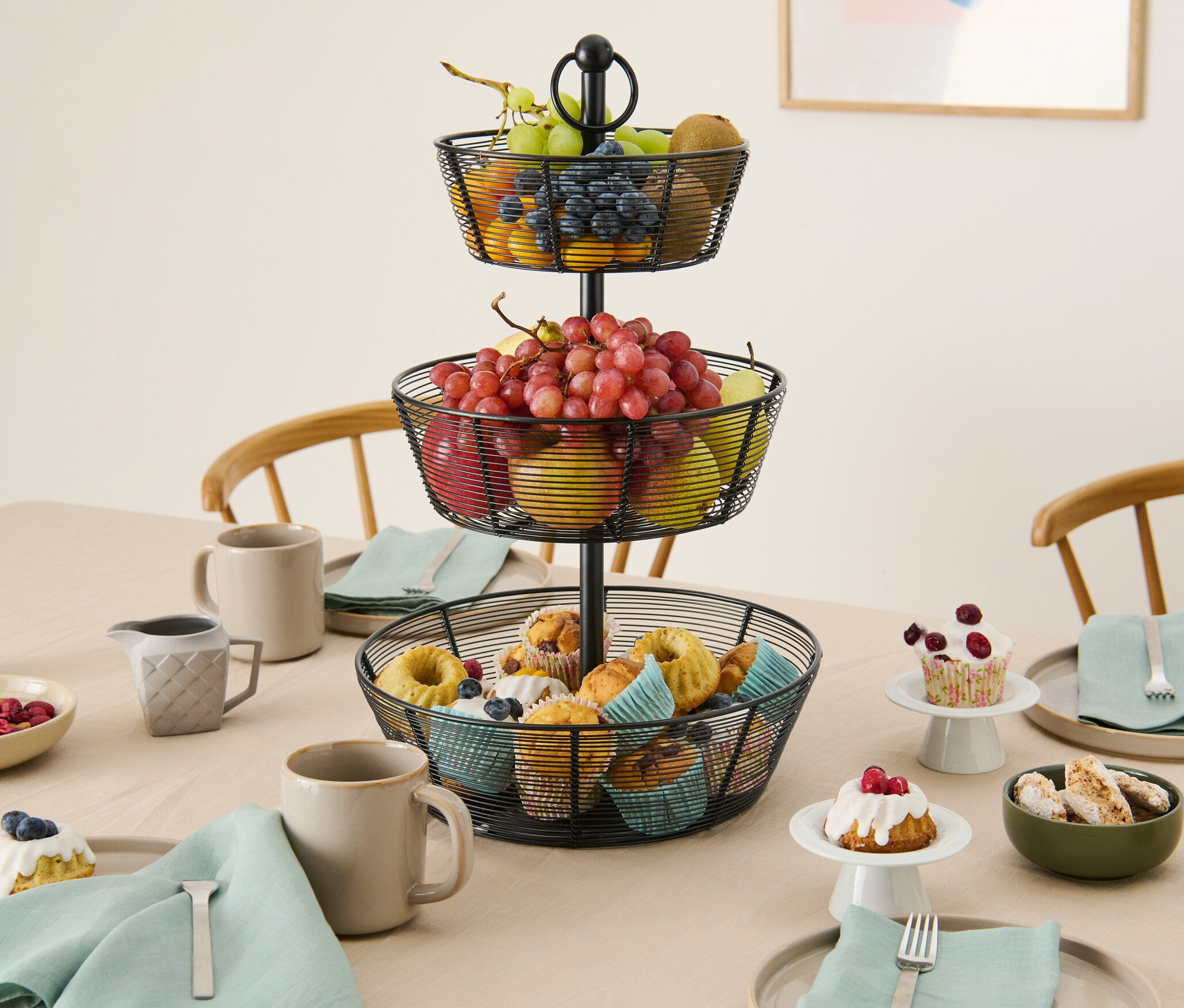 Eine dreistöckige Etagere mit Obst und Muffins steht auf einem Tisch.