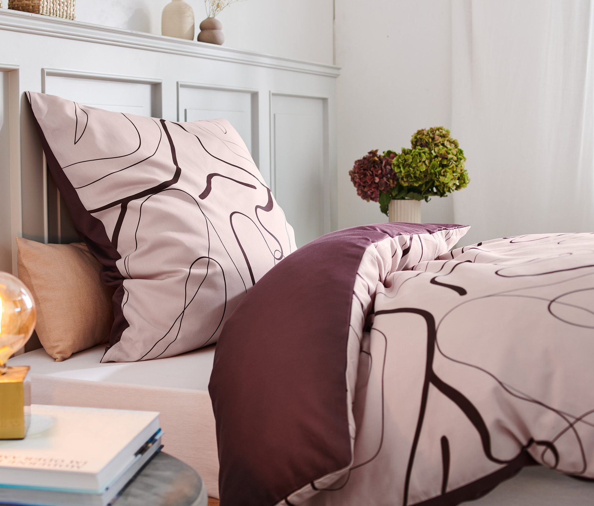 Gemusterte Bettwäsche auf einem Bett neben einer Lampe.