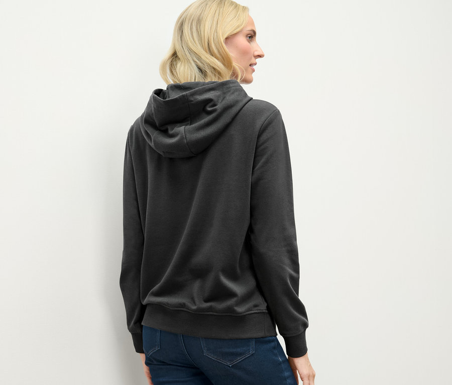 Rückansicht einer blonden Frau im anthrazitfarbenen Hoodie.