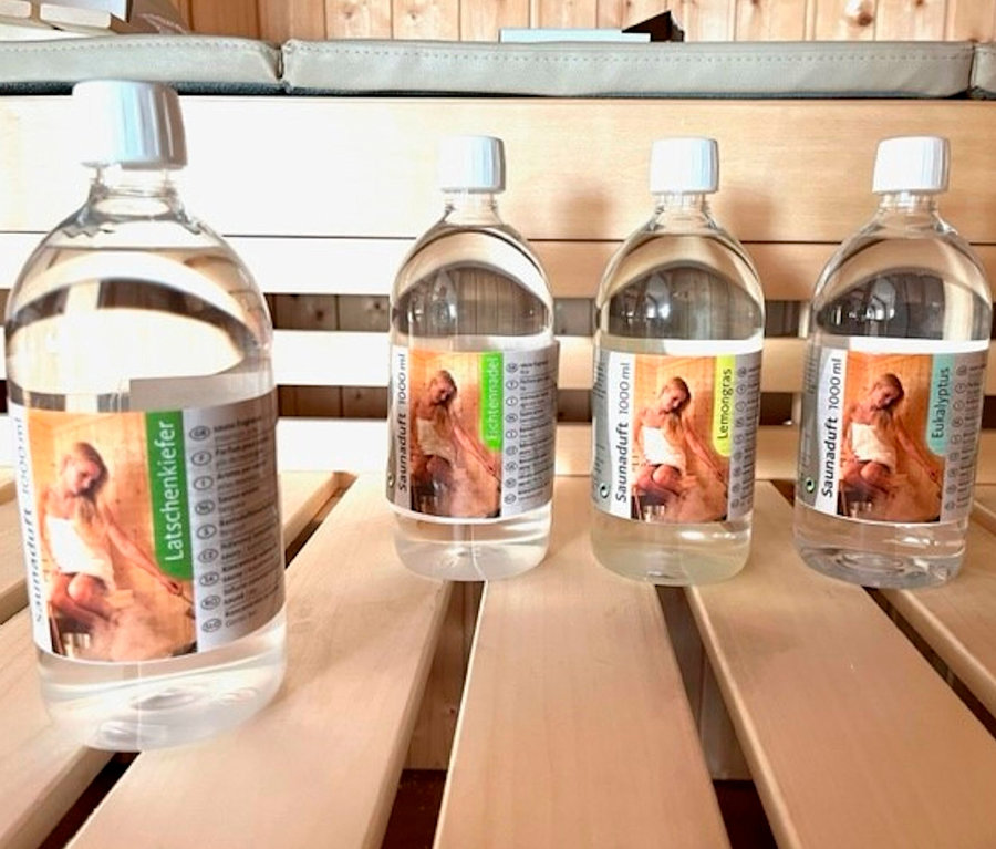 Vier Flaschen Karibu Sauna-Aufgusskonzentrat, 4x 1.000 ml, stehen auf einer hölzernen Saunabank.