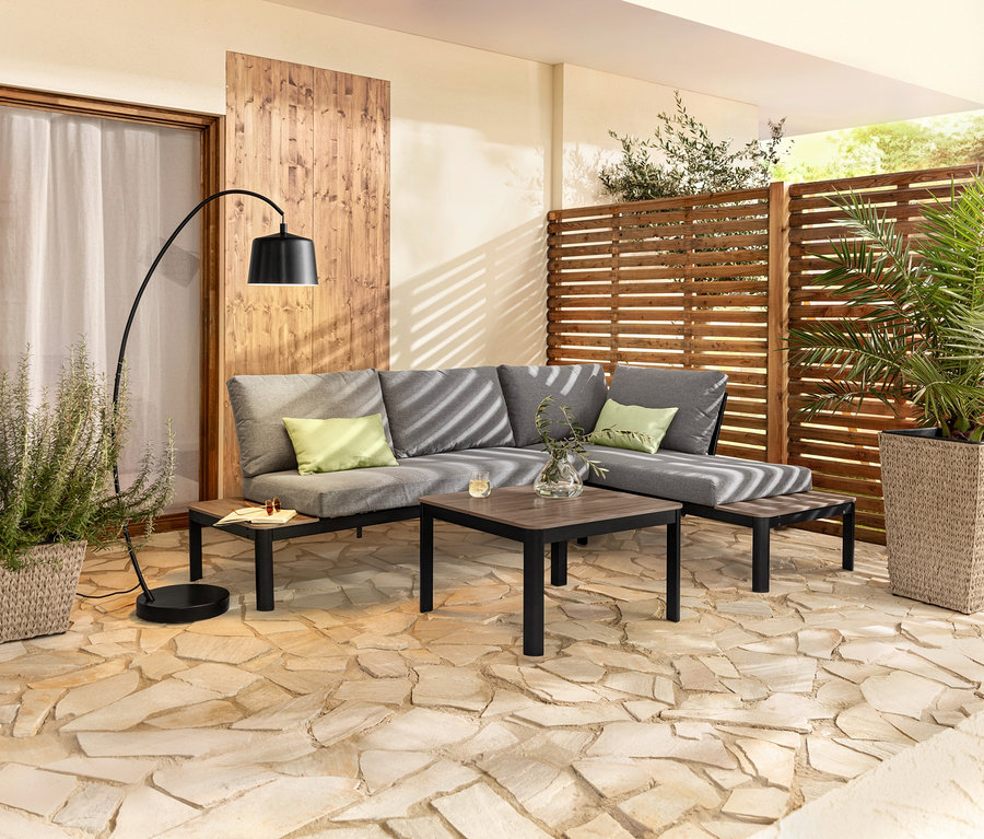Flexible Lounge-Ecke mit Duraboard®-Tischplatten, Bogenleuchte aus Metall, 2 Outdoor-Kissen und 2 Pflanzsäulen mit Fischgrat-Geflecht.