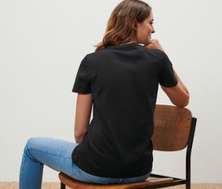 Frau sitzt auf einem Stuhl und trägt ein schwarzes T-Shirt.
