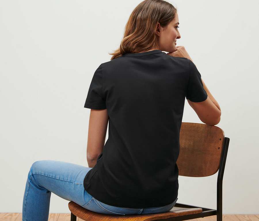 Frau sitzt auf einem Stuhl und trägt ein schwarzes T-Shirt.