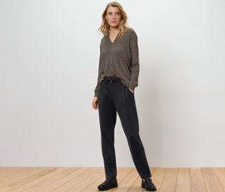 Blonde Frau steht in Joggpants und gemusterter Bluse.