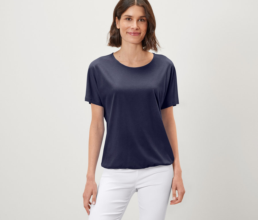 Frau trägt ein hellblaues Blusenshirt und weiße Hosen.