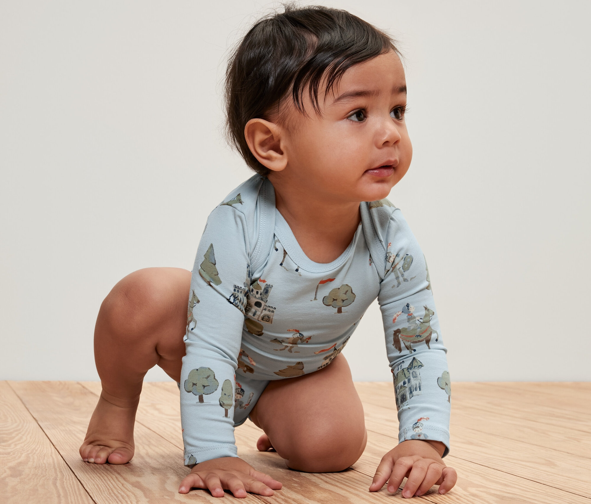 Ein Baby krabbelt auf einem Holzboden und trägt einen hellblauen Babybody mit Ritter-Motiv (5 Stück).