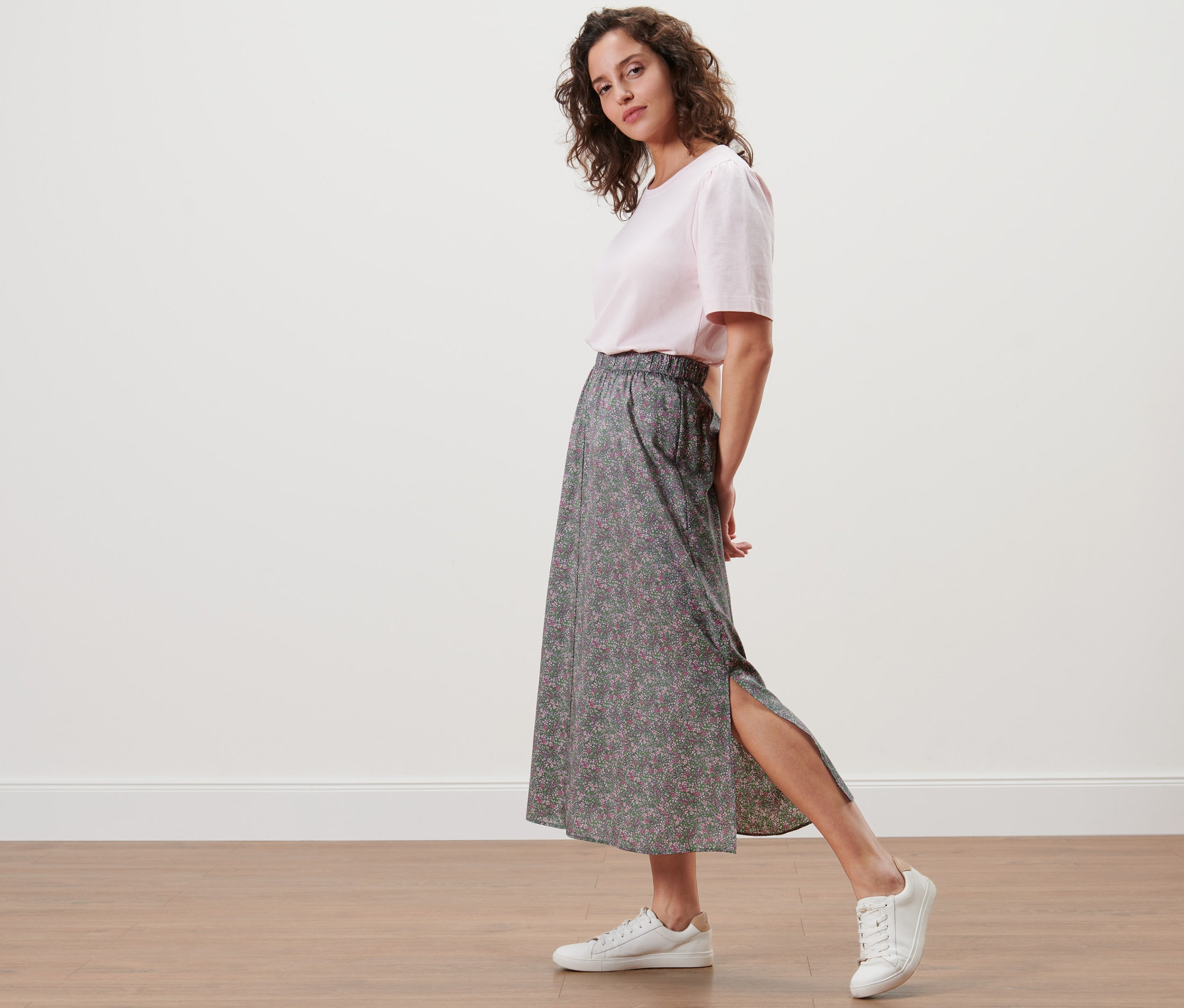 Frau posiert in einem floralen Midi-Rock und weißen Turnschuhen.