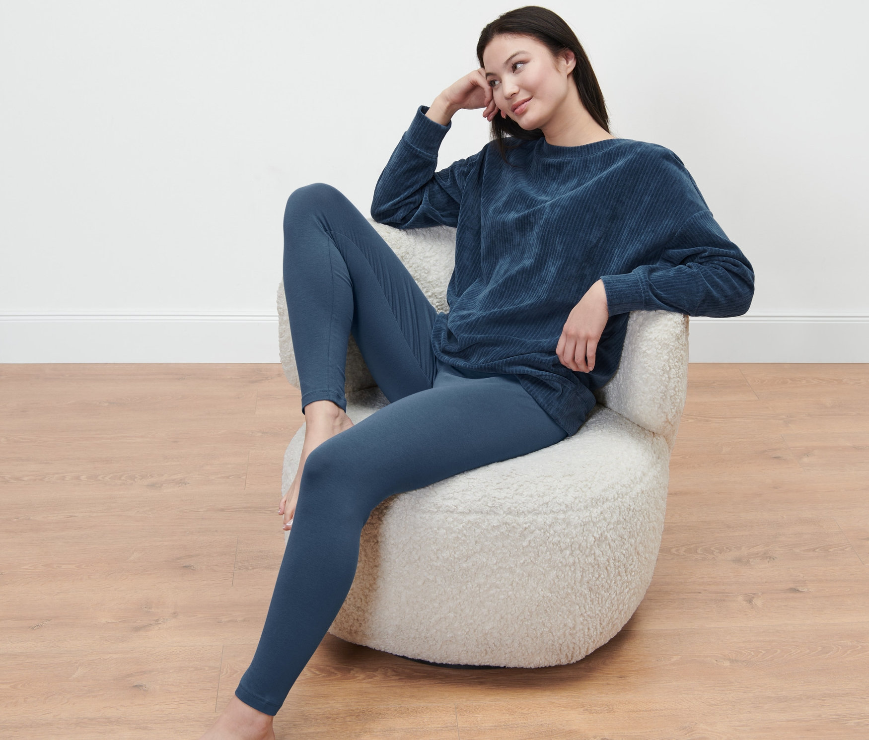 Frau sitzt im Sessel und trägt einen Leggings-Pyjama.