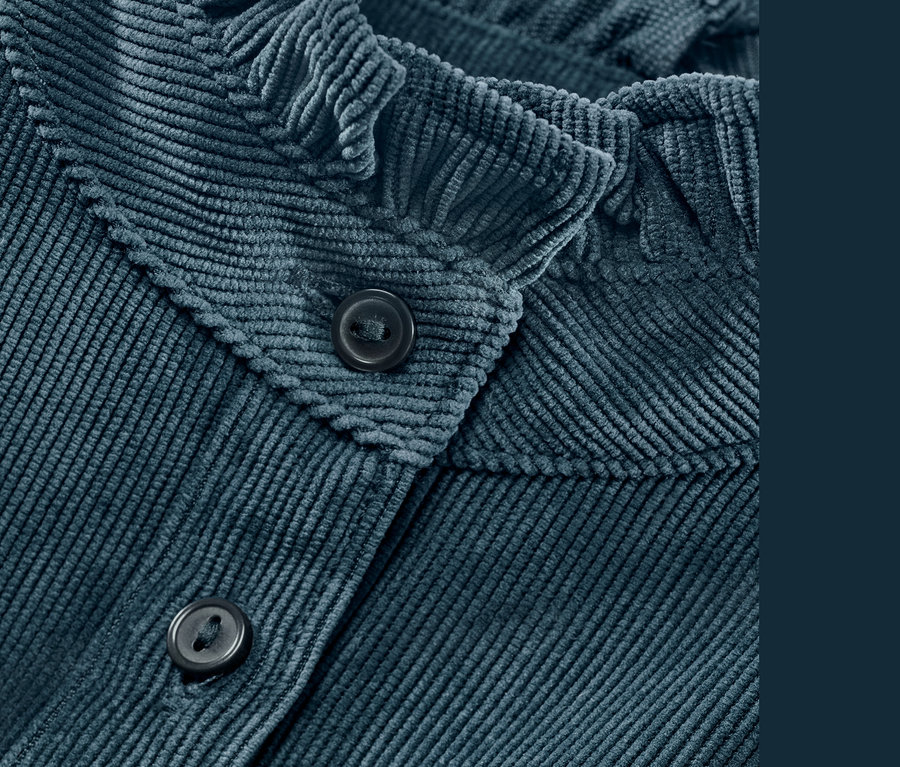 Detailaufnahme einer blauen Cordbluse mit Rüschendetail und Knöpfen.