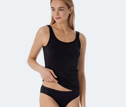 Frau trägt ein schwarzes SCHIESSER Trägertop mit Modal und dezenter Streifenstruktur sowie einen schwarzen Slip. Sie hebt das Top leicht an.