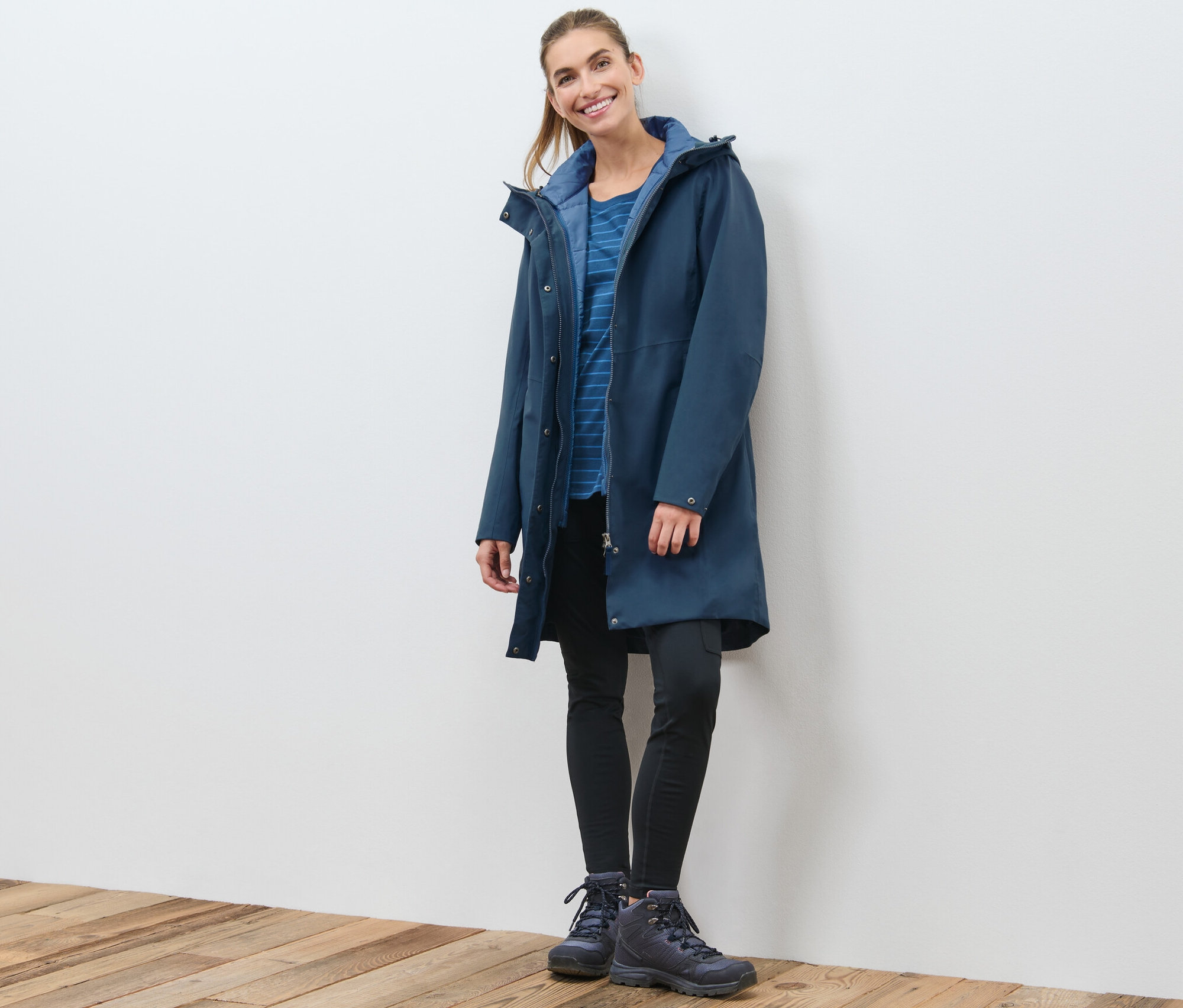 Eine Frau posiert in einem marineblauen 3-in-1-Funktionsmantel mit Weste.