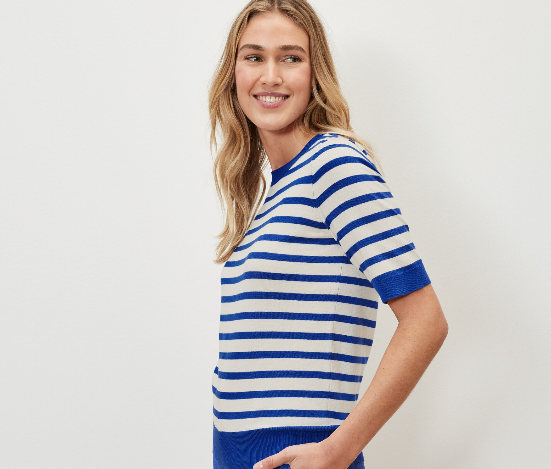 Frau trägt einen gestreiften Feinstrickpullover und blaue Hosen.