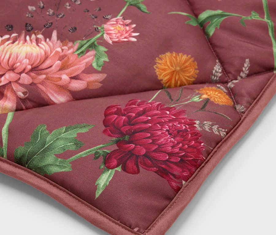 Detailaufnahme einer Ecke einer gesteppten Decke mit einem Blumenmuster in Rot-, Orange- und Grüntönen.