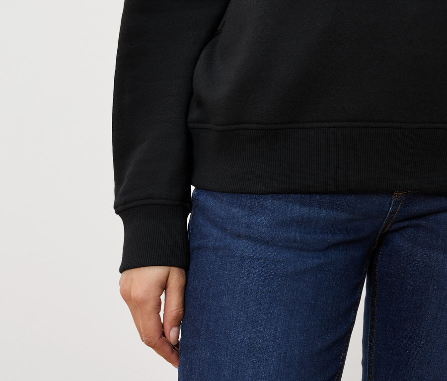 Teilansicht einer Person mit schwarzem Pullover und blauen Jeans.