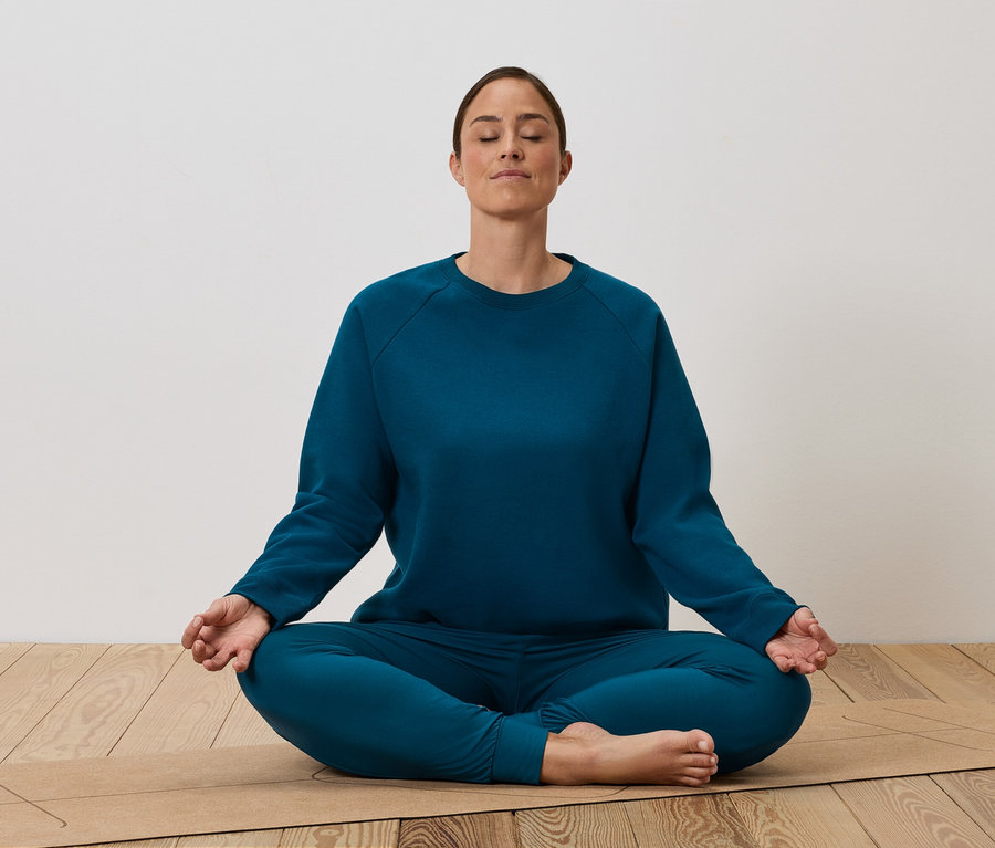 Eine Frau sitzt im Schneidersitz auf einer Yogamatte und meditiert.