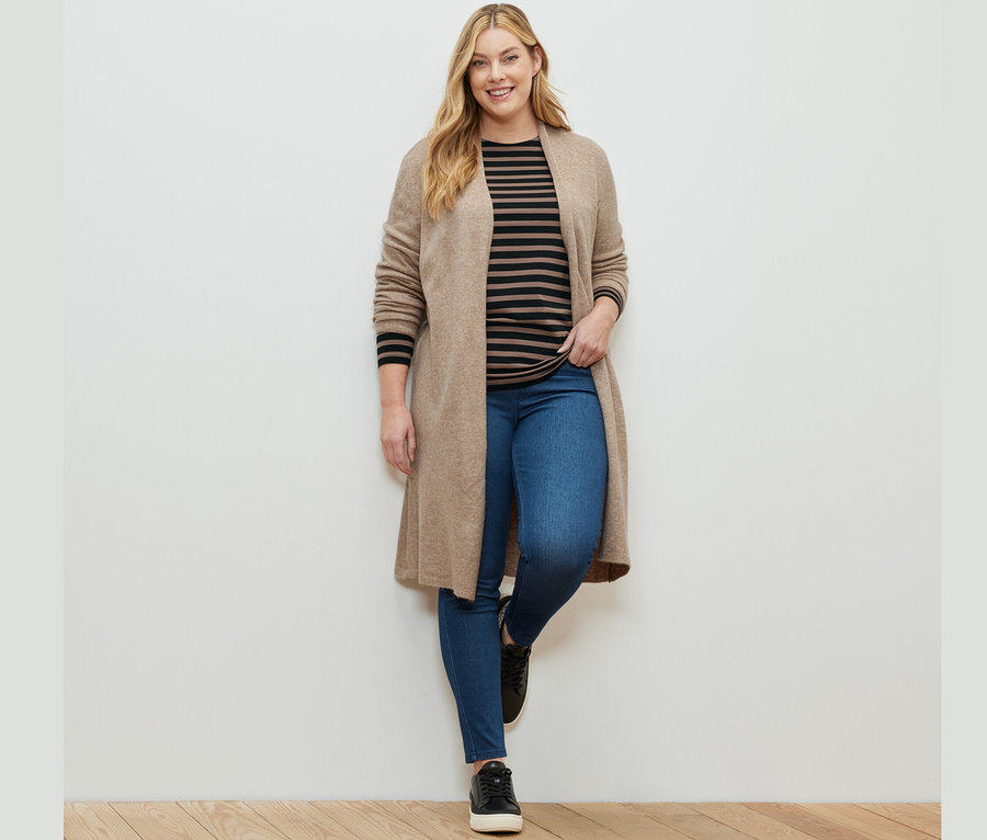 Frau posiert in Jeggings, einem schwarz-braun gestreiften Langarmshirt und einem offenen Longcardigan.