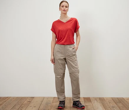 Eine Frau posiert in einer beigen 2-in-1-Funktionshose und einem roten T-Shirt.