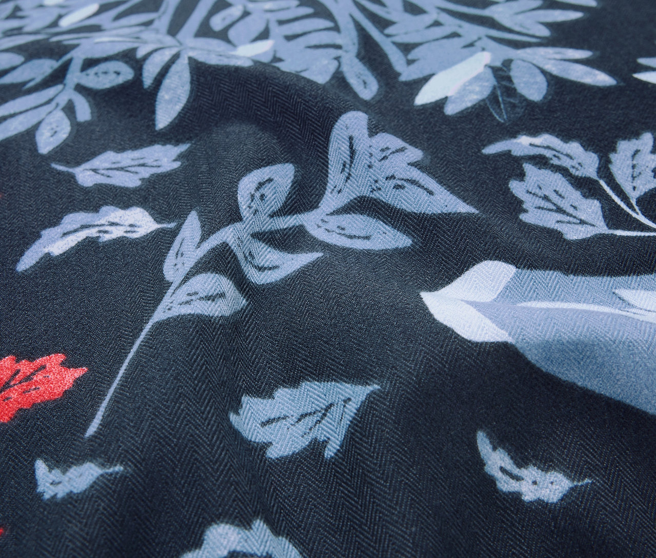 Nahaufnahme eines dunkelblauen Stoffes mit Blatt- und Blumenmuster in Blau- und Rottönen.