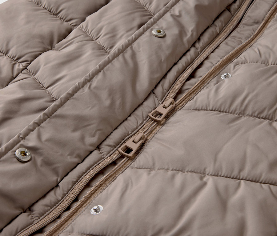 Detail einer beigen Steppjacke mit Reißverschluss und Druckknöpfen.