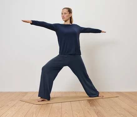 Frau in blauer Kleidung macht Yoga auf einer Matte.