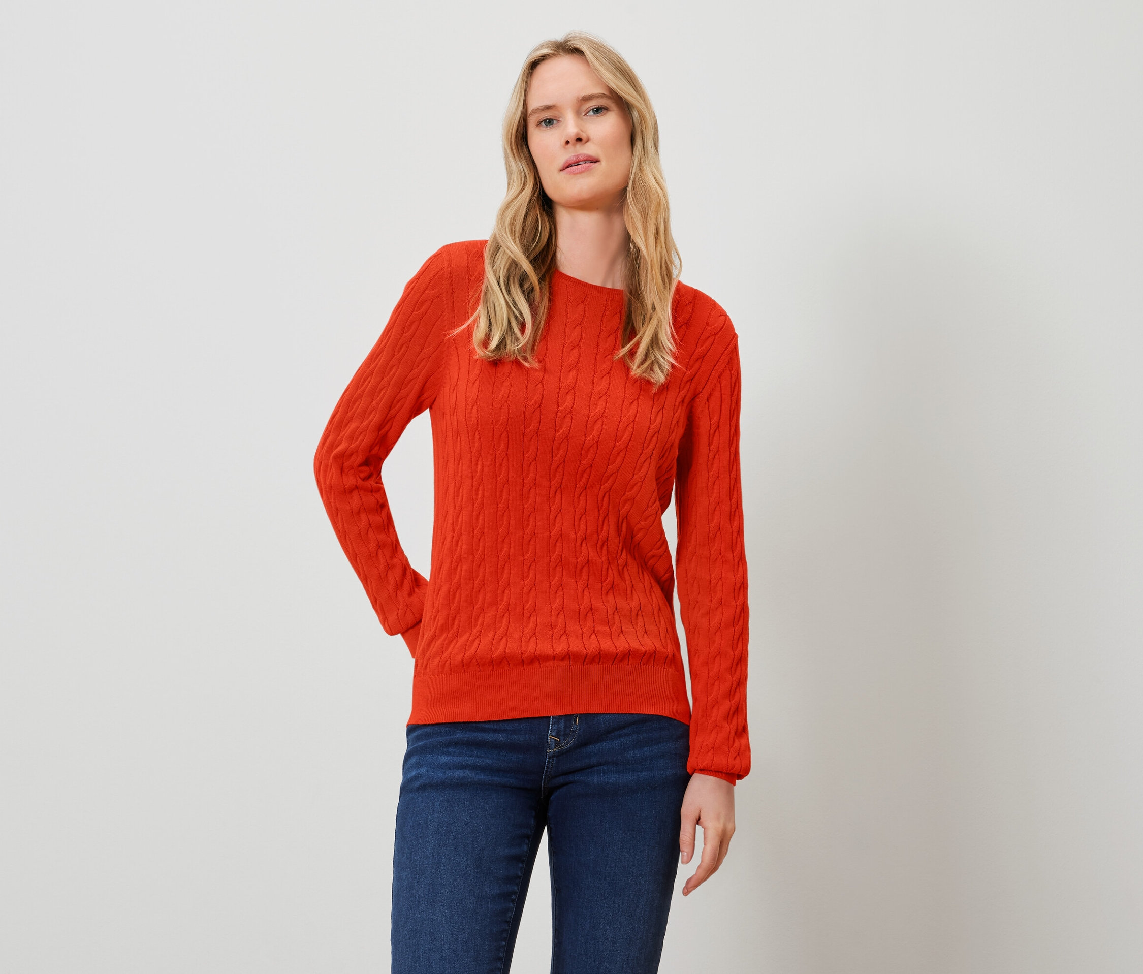 Blonde Frau posiert in orangefarbenem Pullover und Jeans.