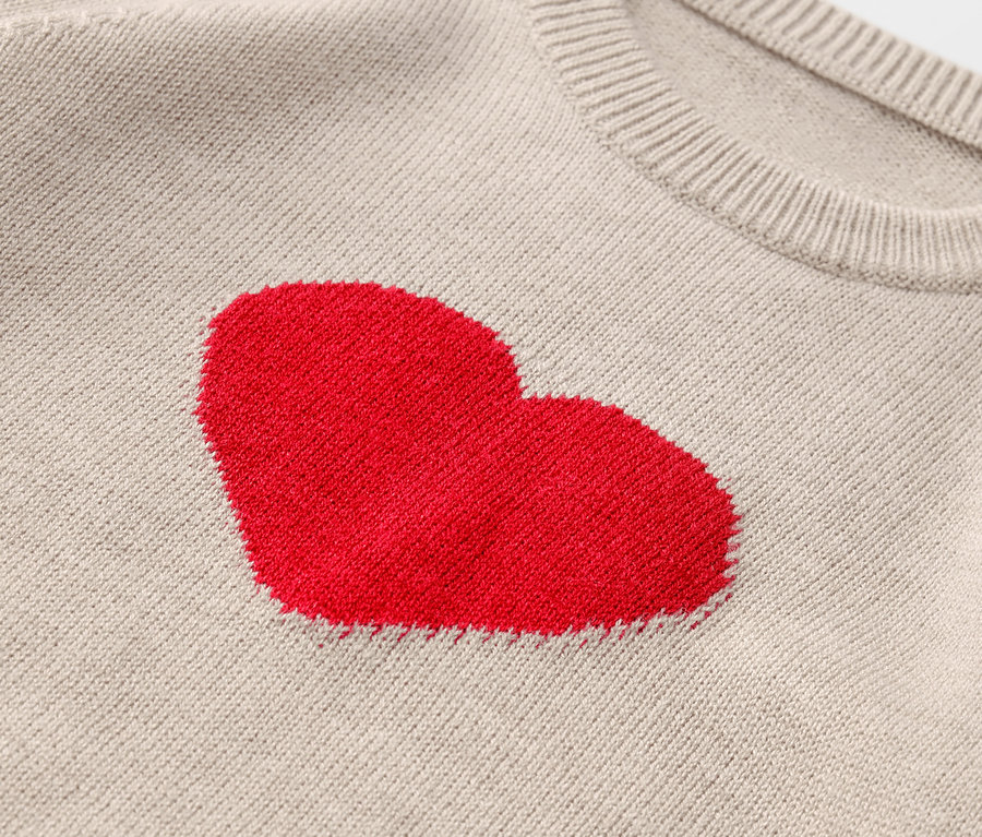 Detailaufnahme eines beigen Pullovers mit rotem Herz.
