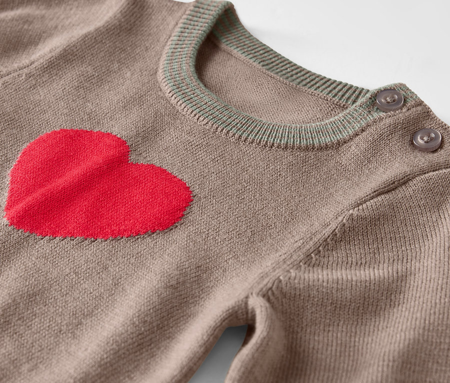 Detailaufnahme eines braunen Pullovers mit rotem Herz auf der Vorderseite und Knöpfen an der Schulter.
