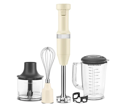 Ein cremefarbener KitchenAid Stabmixer mit Zubehöraufsätzen steht auf einer weißen Oberfläche.
