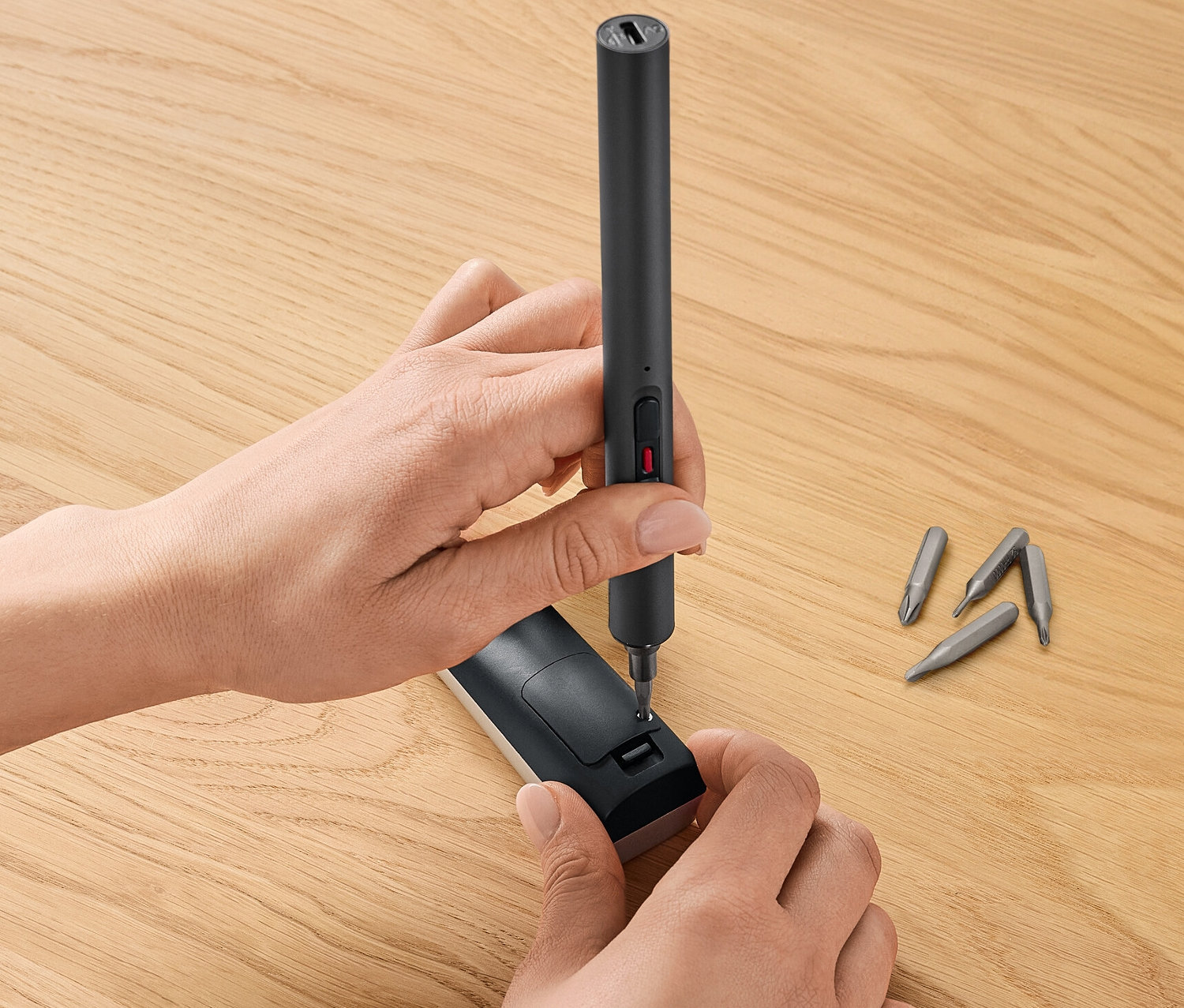 Person lädt Mini-Akku-Schraubendreher-Set auf einem Holztisch auf.